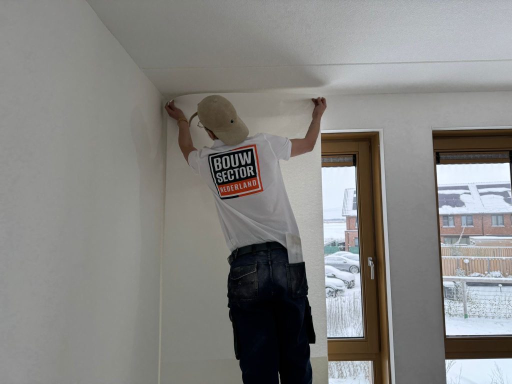 Behanger van Bouwsector Nederland drukt een baan vlies aan tegen het plafond van een nieuwe kamer, buiten ligt sneeuw