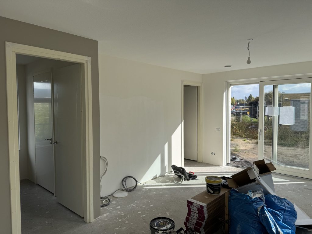 Net opgeleverde woonkamer met kale wanden, tuindeuren en dozen laminaat op de betonvloer