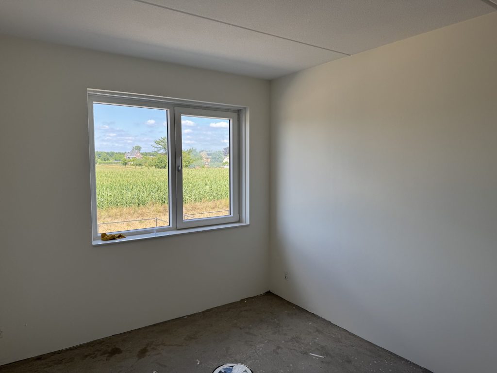 Lege slaapkamer met gladde lichte wanden en een raam met uitzicht over een maisveld