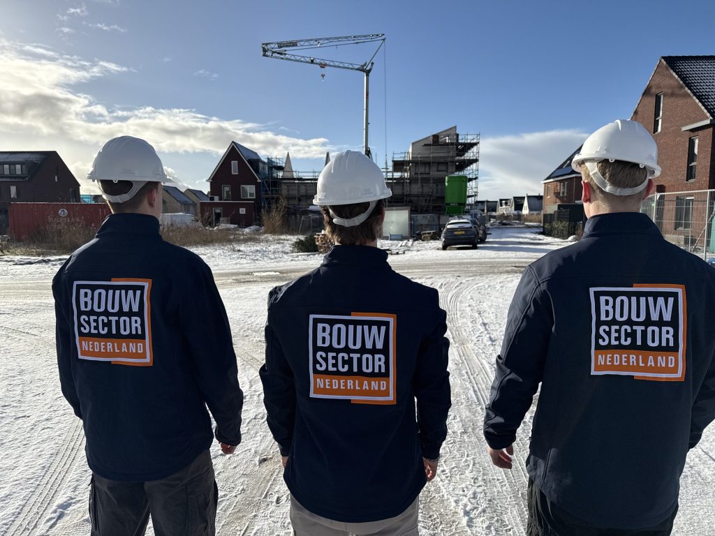 Drie vakmensen van Bouwsector Nederland met witte helm kijken naar een nieuwbouwstraat in aanbouw met een kraan